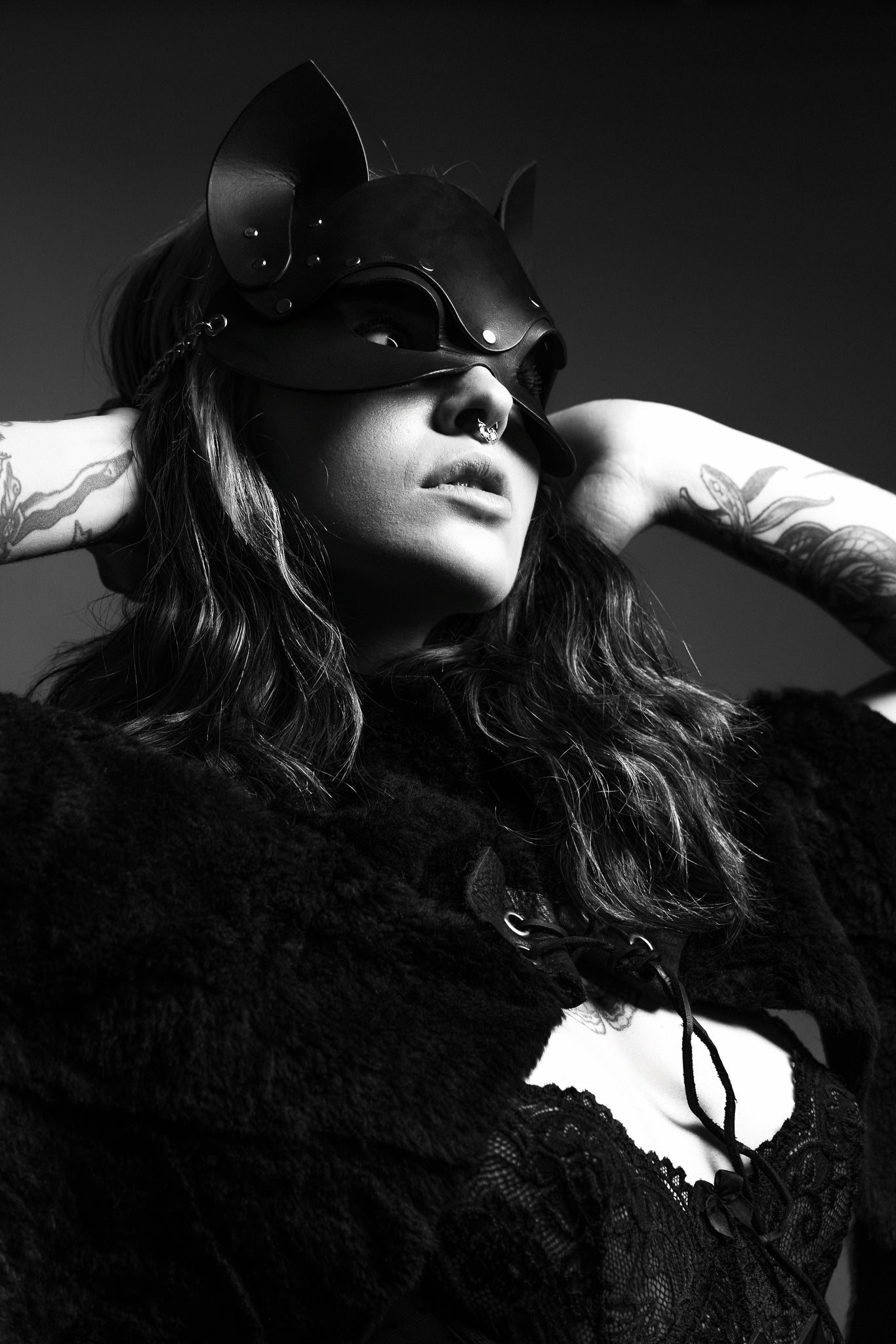 Person wearing a black cat mask and fur coat against a dark background